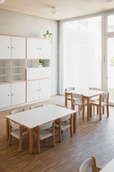 Kinderbistro Kita Kindergartenmöbel und Raumgestaltung: Heller, moderner Essensbereich der Kita mit Möbeln in Buche-Kante aus Echtholz, ausgestattet mit Tischen und Stühlen in unterschiedlichen Höhen für Krippe und Kindergarten.