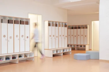 Garderobe mit Türen Kindergartenmöbel und Raumgestaltung: Aufgeräumte Garderobe in der Kita mit individuellen Türen und Stauraum für jedes Kind, ergänzt durch Schaumstoff-Sitzelemente zum Anziehen und Warten.