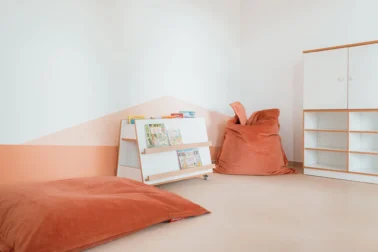 Leseecke mit Bücherwagen und Sitzsack Papoq Rückzugsraum im Kindergarten: Gemütlicher Lese- und Entspannungsbereich mit bequemen Sitzsäcken, kinderfreundlichem Bücherregal und warmer Farbgestaltung für Geborgenheit.