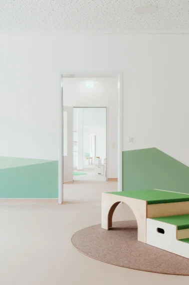 Spielpodest mit Tretford-Teppich Kindergartenmöbel und Raumgestaltung: Spielpodest mit Tretford-Teppich im Durchgang zu den Gruppenräumen einer Kita, fördert Kreativität und Bewegung.